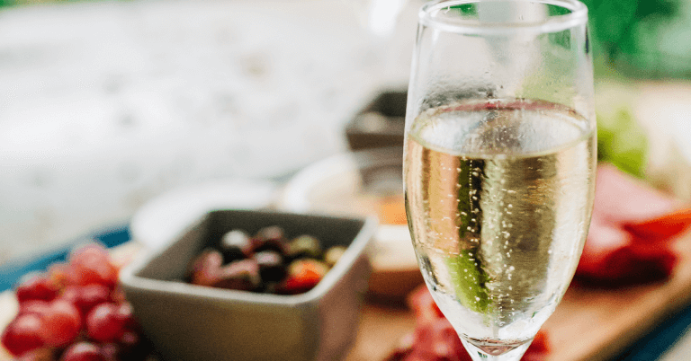 a glass of sparkling wine standing on a table with some snacks in the background